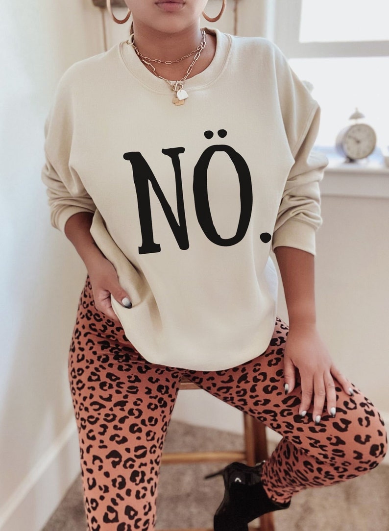 May include: A beige sweatshirt with the word "N&Ouml;." printed in black on the front. The model is wearing leopard print leggings.