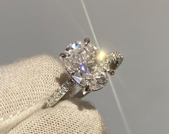 May include: A silver ring with a large, round, clear diamond in the center. The diamond is surrounded by smaller diamonds. The ring is set on a white cloth.
