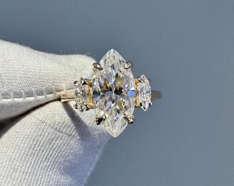 May include: A gold ring with a large marquise-shaped diamond in the center and two smaller marquise-shaped diamonds on either side.