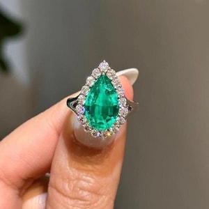 May include: A pear-shaped emerald ring with a halo of smaller diamonds set in white gold.