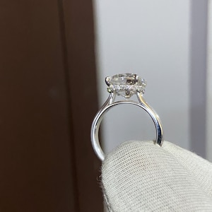 May include: A silver engagement ring with a large, round, clear diamond center stone surrounded by a halo of smaller diamonds. The ring is set on a thin band.