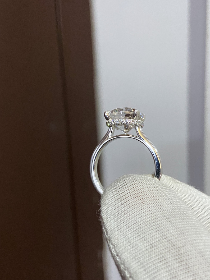 May include: A silver engagement ring with a large, round, clear diamond center stone surrounded by a halo of smaller diamonds. The ring is set on a thin band.