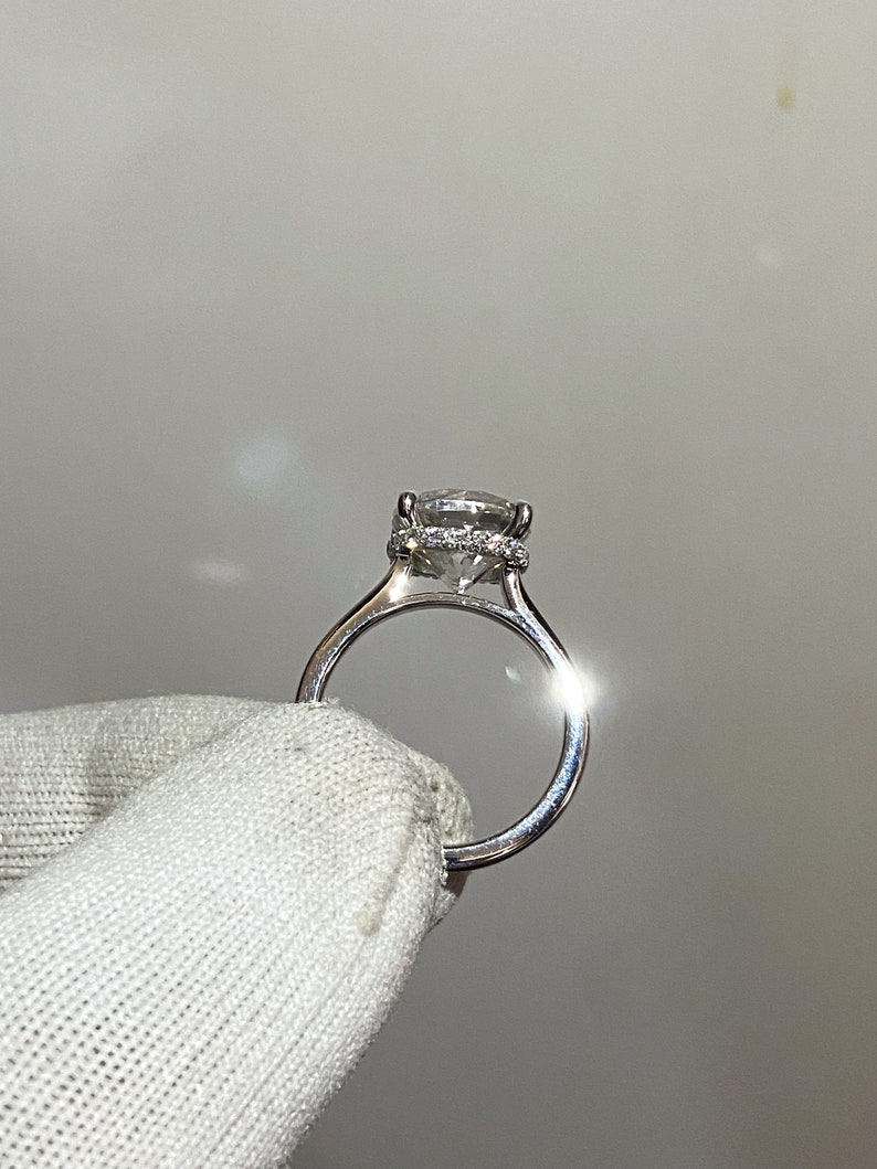 May include: A silver engagement ring with a large, clear, round-cut diamond center stone. The diamond is surrounded by a halo of smaller diamonds. The ring band is also set with smaller diamonds.