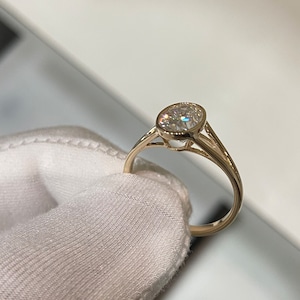 Op de afbeelding: Een gouden ring met een bezel-setting met een ronde, heldere edelsteen.