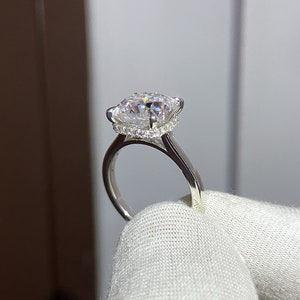 May include: A silver ring with a large, clear, square-shaped diamond set in a halo of smaller diamonds.
