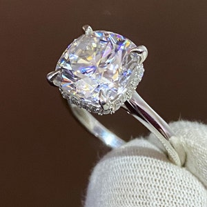 May include: A silver ring with a large, clear, cushion-cut diamond center stone surrounded by a halo of smaller diamonds.