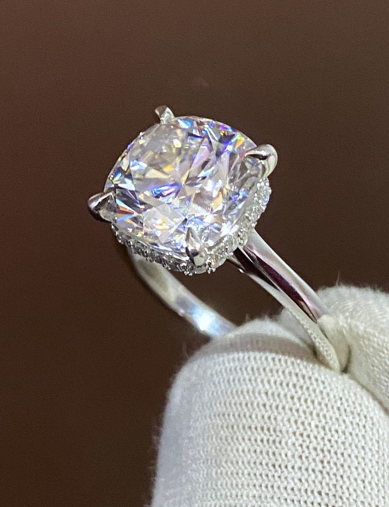 May include: A silver ring with a large, clear, cushion-cut diamond center stone surrounded by a halo of smaller diamonds.