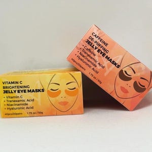 May include: Two boxes of jelly eye masks are displayed. One box is labeled "Vitamin C Brightening Jelly Eye Masks" and the other "Caffeine De-Puffing Jelly Eye Masks." Each box features a face with eye mask illustrations and product information. Each box contains 40 pieces/20 pairs and 1.75 oz/50g.