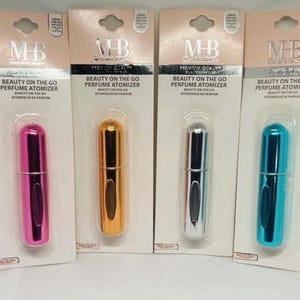May include: Four perfume atomizers in pink, gold, silver, and teal, each packaged on a white card. The cards have the text "MB" and "BEAUTY ON THE GO PERFUME ATOMIZER". The atomizers are cylindrical and designed for travel.