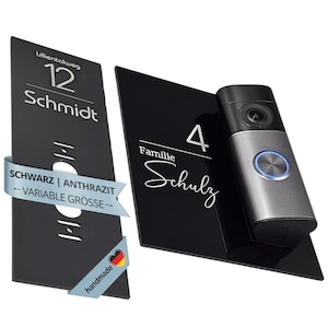 Könnte beinhalten: Zwei schwarze rechteckige Türschilder mit weißer Schrift. Ein Schild zeigt 'Lillientalweg 12 Schmidt', das andere 'Familie 4 Schulz' mit einer silber-schwarzen Videotürklingel. Ein hellblaues Banner trägt die Aufschrift 'SCHWARZ | ANTHRAZIT VARIABLE GRÖSSE'.