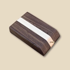 May include: A wooden box with a white stripe and a brass pin on the side. The box is made of dark wood and has a smooth finish.