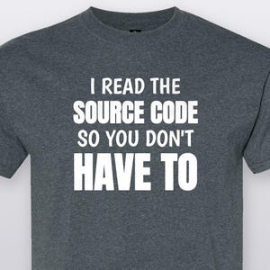 May include: A dark heather grey short-sleeved t-shirt featuring white text printed on the chest that reads: I READ THE SOURCE CODE SO YOU DON'T HAVE TO. The garment has a crew neckline and a standard fit, constructed from a soft, textured fabric.