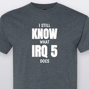May include: A dark heather gray short-sleeved t-shirt featuring white text printed on the chest that reads I STILL KNOW WHAT IRQ 5 DOES. The shirt has a crew neckline and a standard fit, constructed from a soft, heathered fabric blend.