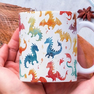 Peut inclure: Une tasse en céramique blanche avec un motif de dragon coloré. La tasse est tenue par les mains d'une personne.