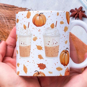 May include: White ceramic mug with a fall-themed design. The mug features a repeating pattern of orange pumpkins, brown leaves, and white coffee cups with whipped cream and a sprinkle of cinnamon.