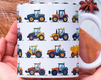 Könnte beinhalten: Eine weiße Keramiktasse mit einem Muster aus gelben, orangefarbenen und blauen Traktoren auf weißem Hintergrund. Die Tasse wird von den Händen einer Person gehalten.