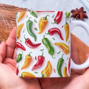 Può includere: Una tazza in ceramica bianca con un motivo colorato di peperoncini rossi, gialli e verdi. La tazza è tenuta dalle mani di una persona.
