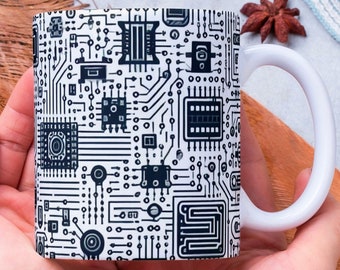 Puede incluir: Una taza de cerámica blanca con un diseño de placa de circuito negro y blanco. La taza está siendo sostenida en dos manos.