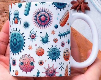 Puede incluir: Taza de cerámica blanca con un patrón colorido de varias bacterias y microorganismos. La taza está siendo sostenida por las manos de una persona.