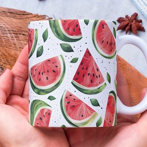 May include: White ceramic mug with a watermelon print. The mug is being held by a person's hands.