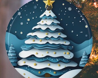May include: A round Christmas ornament with a winter scene. The ornament features a layered paper-cut design of a Christmas tree in white and blue, with gold star accents. A gold star tops the tree, and the ornament hangs from a gold string.