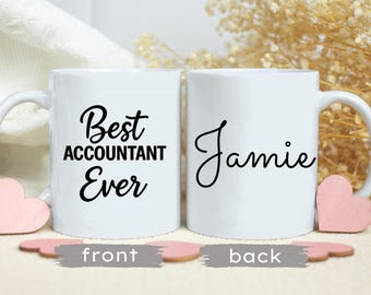 Może przedstawiać: Dwa białe ceramiczne kubki z czarnym tekstem. Jeden kubek mówi "Best ACCOUNTANT Ever", a drugi "Jamie". Różowe dekoracje w kształcie serca są przymocowane do uchwytów. Kubki stoją na jasnej powierzchni.