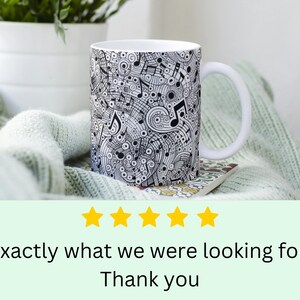 May include: White ceramic mug with a black and white design of musical notes and swirls. The mug has a handle and is sitting on a light green knitted blanket.