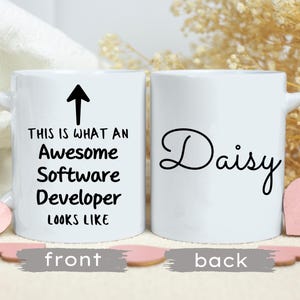 Może przedstawiać: Biały kubek ceramiczny z czarną strzałką skierowaną w górę i tekstem "This is what an awesome software developer looks like". Na odwrotnej stronie kubka widnieje imię "Daisy" napisane czarnym kursywą.