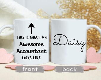 Może przedstawiać: Biały kubek ceramiczny z czarną strzałką skierowaną w górę i tekstem "This is what an awesome accountant looks like". Na odwrotnej stronie kubka widnieje imię "Daisy" napisane czarnym kursywą.
