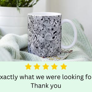 Puede incluir: Taza de cer&aacute;mica blanca con un dise&ntilde;o en blanco y negro de notas musicales y remolinos. La taza tiene un asa y est&aacute; sentada sobre una manta de punto verde claro.