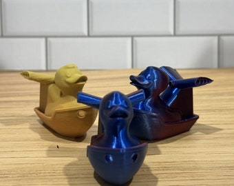 May include: Three 3D printed rubber duck toys. One yellow duck is in a boat, one blue duck is in a boat, and one blue duck is in a boat with a propeller.