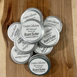 Op de afbeelding: Een stapel zilveren blikken met etiketten waarop staat "Creative Collections All Natural Food Safe Board Butter creativecollections03@gmail.com".