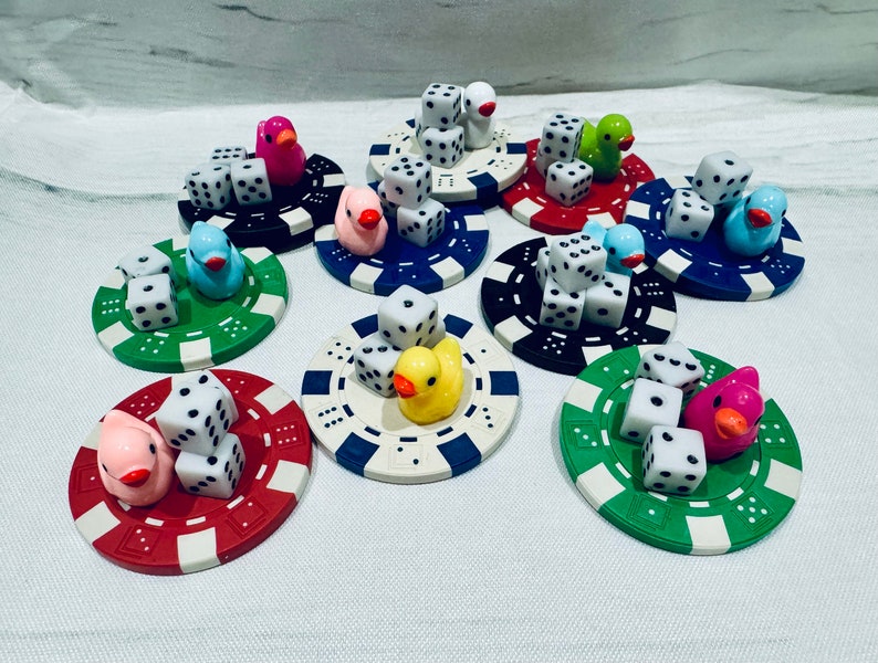Puede incluir: Nueve fichas de casino de colores con dados y figuras de patos de goma en la parte superior. Cada ficha tiene un color y un dise&ntilde;o diferente.
