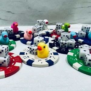 Puede incluir: Un conjunto de nueve figuras de patos coloridos con dados encima. Cada pato est&aacute; sentado sobre una base circular de color y dise&ntilde;o diferentes. Los patos son de diferentes colores, incluyendo rosa, azul, amarillo y verde.