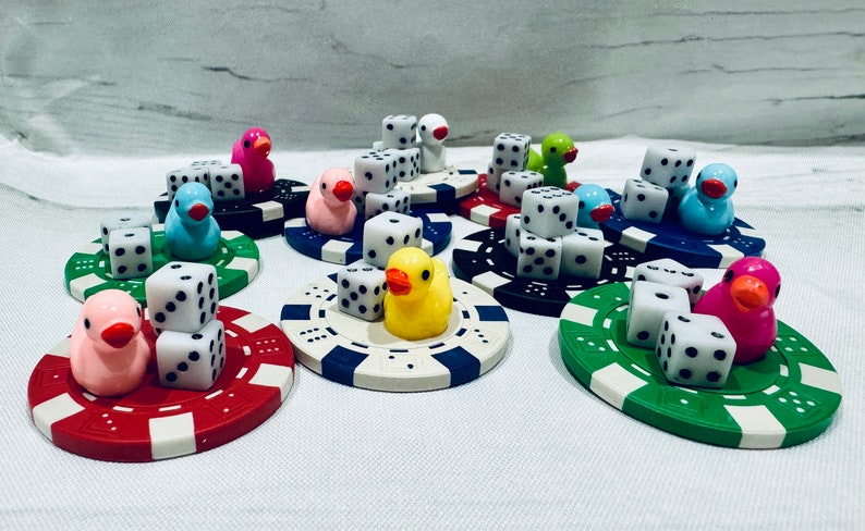 Puede incluir: Un conjunto de nueve figuras de patos coloridos con dados encima. Cada pato est&aacute; sentado sobre una base circular de color y dise&ntilde;o diferentes. Los patos son de diferentes colores, incluyendo rosa, azul, amarillo y verde.