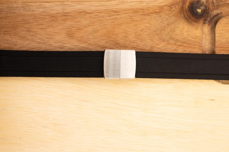 Puede incluir: Una correa de reloj de caucho negro con una hebilla plateada.