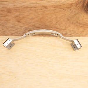 May include: A silver metal watch band clasp with a hinged design. The clasp is open and ready to be attached to a watch band.