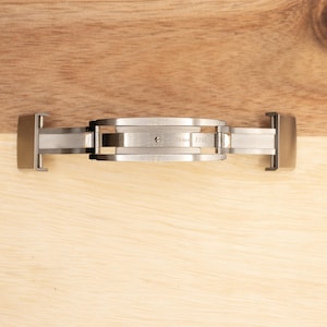 May include: A silver watch band clasp with a push-button release mechanism.