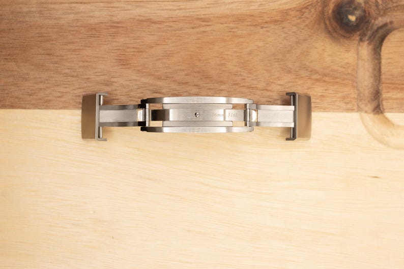 May include: A silver watch band clasp with a push-button release mechanism.
