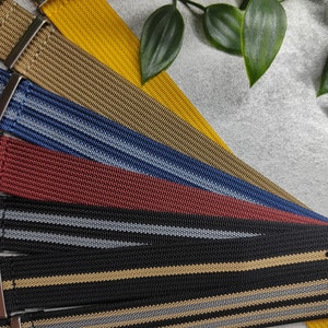 Peut inclure: Cinq bracelets de montre différents, chacun avec une couleur et un motif différents. Les bracelets sont en nylon tissé et ont des boucles métalliques. Les bracelets sont disposés en éventail, le bracelet jaune en haut et le bracelet noir en bas.