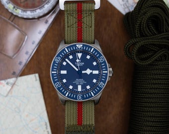 May include: A stainless steel wristwatch with a blue dial and a green and red striped nylon strap. The watch is set against a backdrop of a compass and a map, suggesting an outdoor or adventure theme.