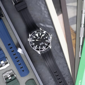 May include: A black Omega Seamaster watch with a black rubber strap. The watch has a black dial with white markings and a silver bezel. Additional blue and green watch straps are visible.