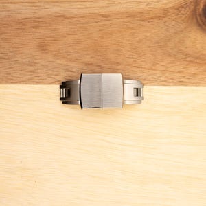 May include: A silver watch band clasp with a brushed finish.
