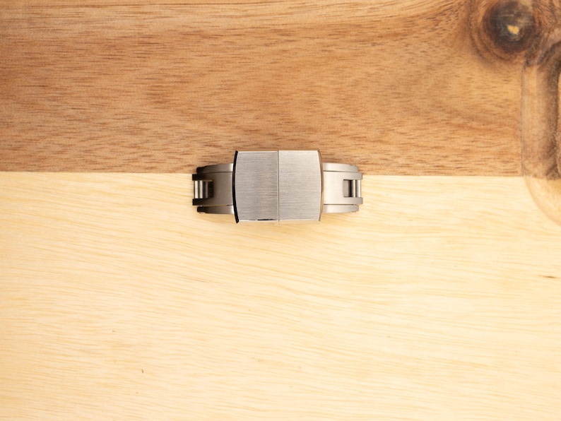 May include: A silver watch band clasp with a brushed finish.