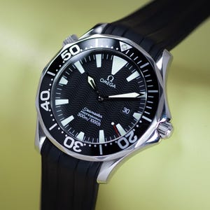 May include: A stainless steel Omega Seamaster Professional watch with a black dial and a black rubber strap. The watch face features white luminous markers and hands, with the text "OMEGA" and "Seamaster PROFESSIONAL 300m/1000ft". The watch is water resistant to 1000 feet.