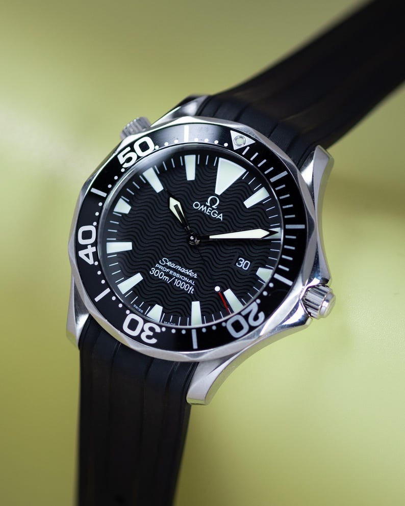 May include: A stainless steel Omega Seamaster Professional watch with a black dial and a black rubber strap. The watch face features white luminous markers and hands, with the text "OMEGA" and "Seamaster PROFESSIONAL 300m/1000ft". The watch is water resistant to 1000 feet.