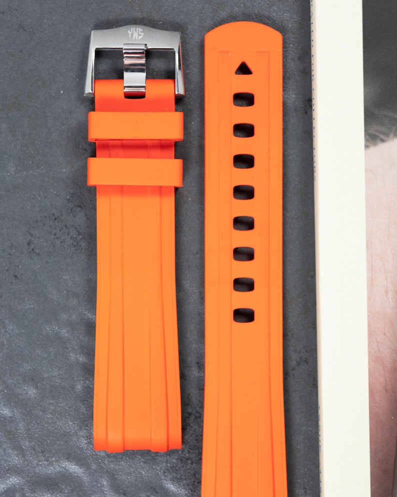 May include: Bright orange watch strap with a silver buckle. The strap is made of a flexible material and features a series of holes for adjustment. The buckle is engraved with the letters "YWS".
