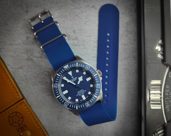 May include: A blue rubber watch strap with silver hardware and a blue watch face with white markings. The watch face says "TUDOR" and "PELAGOS".