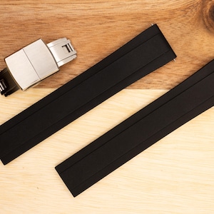 Puede incluir: Dos correas de reloj de caucho negro con una hebilla plateada. Las correas tienen una superficie texturizada y est&aacute;n dise&ntilde;adas para un reloj.