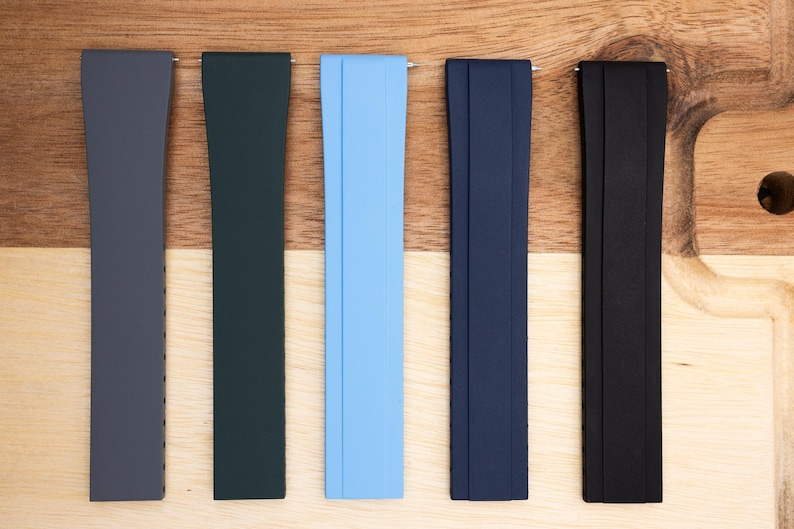 May include: Five different colored watch bands. The bands are made of a rubber-like material and are in the colors gray, dark green, light blue, dark blue, and black.